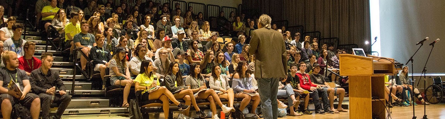 a presenter speaks in front of students in a lecture hall